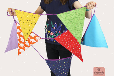 Nahaufnahme einer Person, die eine bunte, handgefertigte Stoff-Wimpelkette mit verschiedenen Mustern hält.