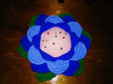 Gehäkeltes Nadelkissen in Blumenform, blau-grün, mit rosa Mitte und bunten Stecknadeln