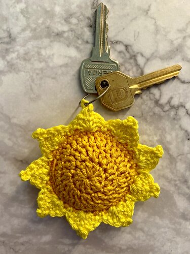 Gehäkelter gelber Sonnenblumen-Schlüsselanhänger an einem Schlüsselbund auf marmoriertem Untergrund.