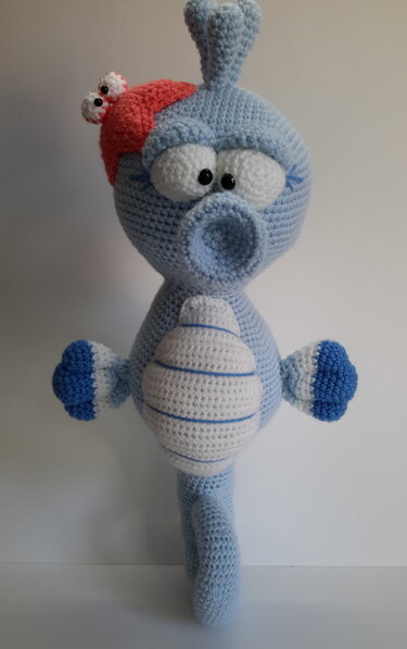 Hellblaues gehäkeltes Seepferdchen-Amigurumi mit weiß gestreiftem Bauch und roter Mütze