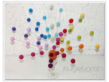 Bunte Häkelkugeln auf dünnen Drähten, fächerförmig aus einem umhäkelten Glas