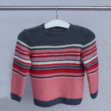 Gestrickter Kinderpullover mit Querstreifen in Rosa, Rot, Grau und Weiß an einem Kleiderbügel