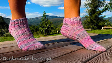 Pair of ankle-length pink and purple variegated knitted socks on a wooden deck