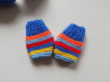 Gestrickte Baby-Fäustlinge mit bunten Querstreifen auf hellem Untergrund