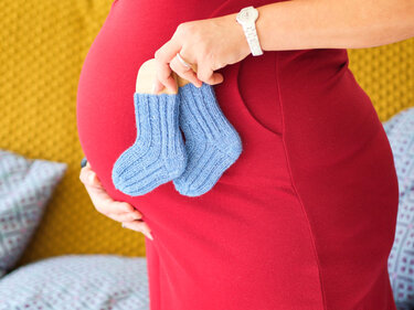 Schwangere Frau hält blaue gestrickte Babysocken vor dem Bauch