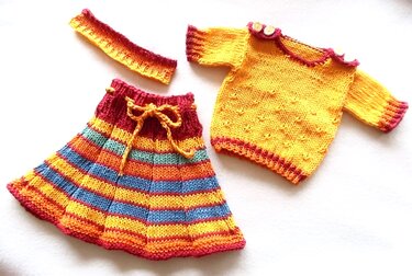 Handgestricktes Kinder- oder Puppenoutfit mit gelbem Pullover, gestreiftem Rock und Stirnband auf weißem Hintergrund.