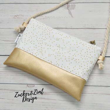 Weiß-goldene Clutch mit feinen goldenen Dreiecken und goldfarbenem Unterteil, mit dickem Seilriemen auf hellem Holzhintergrund.