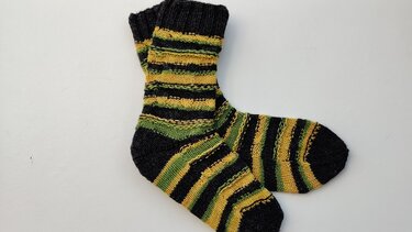 Ein Paar gestrickte Socken mit schwarzen, gelben und grünen Streifen auf hellem Hintergrund