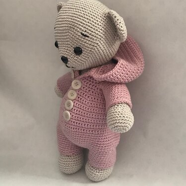 Hand-crocheted teddy bear wearing a pink hooded romper with four white buttons