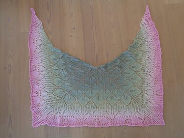 Dreieckstuch mit Blatt-Lochmuster und Farbverlauf von Rosa zu Grün auf Holzboden.