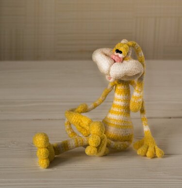 Gehäkelter gelb-weiß gestreifter Osterhase mit langen Ohren sitzt auf einer hellen Holzoberfläche.