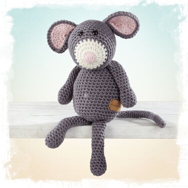 Gehäkelte graue Amigurumi-Maus mit rosafarbenen Ohren und weißer Schnauze auf heller Holzfläche