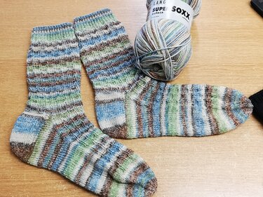 Paar gestreifter handgestrickter Socken mit mehrfarbigem Garnknäuel auf Holztisch