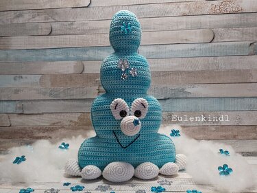Dreiteiliges türkis-weißes Amigurumi mit weißen Applikationen und blauen Blumenakzenten