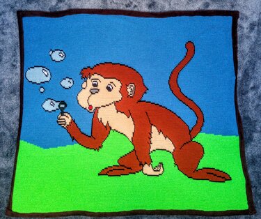 Gehäkelte Babydecke im Pixelmuster mit Affen, der Seifenblasen pustet
