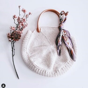 Runde gehäkelte Henkeltasche in Creme mit hellbraunem Griff und gebundenem Tuch