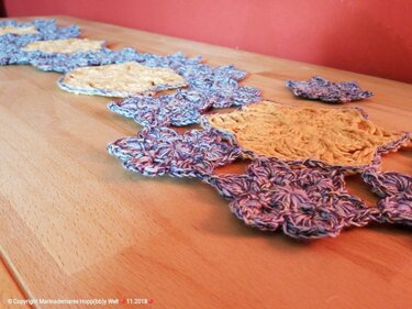 Gehäkelter Tischläufer mit gelben Quadraten und blauen Blütenmotiven auf hellem Holztisch