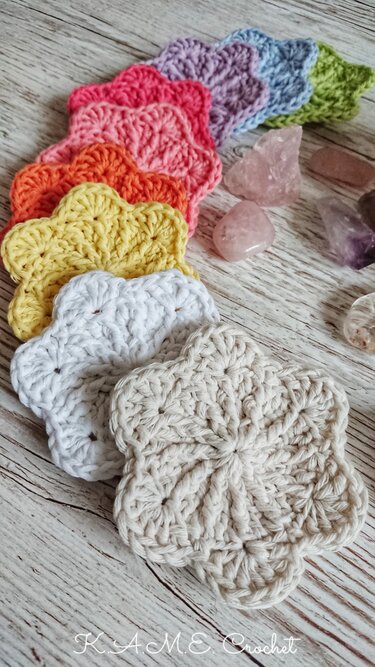 Row of colorful crocheted flower-shaped motifs on a light wooden surface with tumbled stones nearby.