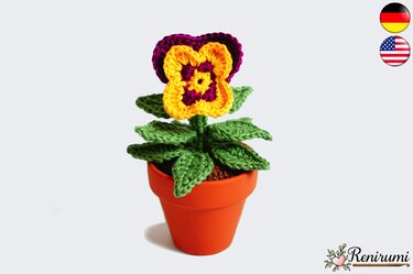 Crocheted pansy with yellow and purple petals and green leaves in a small terracotta pot