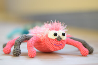 rosa gehäkelte Amigurumi-Spinne mit weißen Augen und grauen Beinen