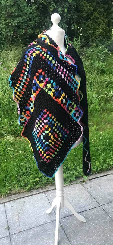 Schwarzer, gehäkelter Schal mit bunten Granny-Squares auf einer Schaufensterpuppe im Garten