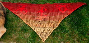 Gehäkeltes rotes bis orangefarbenes Dreieckstuch mit Drachenmotiven auf Gras
