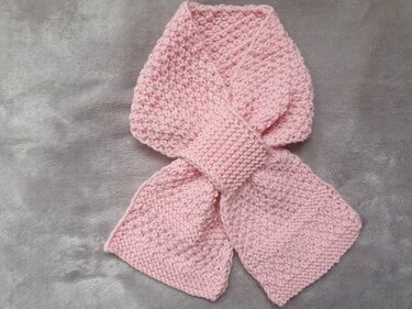 Gestrickter rosa Babyschal mit Durchziehschlaufe auf grauem Hintergrund