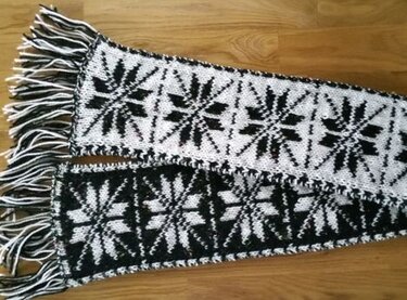 Gestrickter schwarz
weißer Schal mit wiederholtem Sternmuster und Fransen, beide Farbausführungen sichtbar
