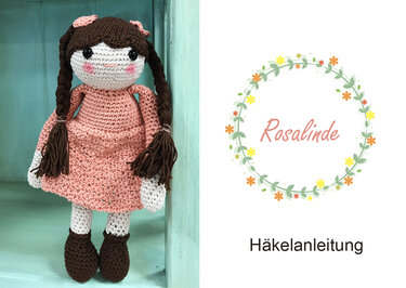 Nostalgische gehäkelte Puppe mit Zöpfen und pastellrosa Kleid neben dem floralen Logo 'Rosalinde Häkelanleitung'.