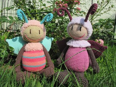 Zwei gehäkelte Amigurumi-Insekten mit Fühlern und Flügeln sitzen im Gras