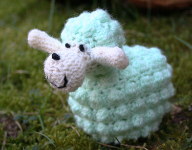 Mintgrünes Amigurumi-Schaf mit ecrufarbenem Kopf und Noppenkörper