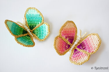 Zwei gehäkelte Schmetterlinge in Türkis und Rosa mit goldener Umrandung und Perlenkörpern