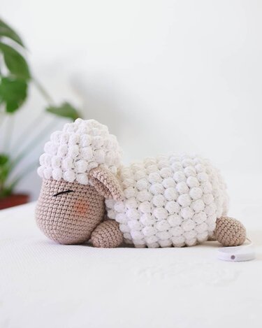 Crocheted amigurumi sleeping lamb with white bobble body and beige head