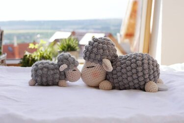 Two grey and cream crocheted amigurumi sheep, large and small, on a white surface.