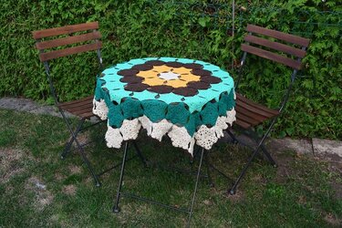 Rundes mehrfarbiges Häkeldeckchen mit floralem Muster auf kleinem Gartentisch