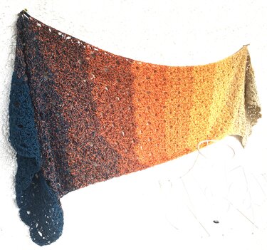 Gehäkelter Schal mit Ombré-Verlauf in Blau, Orange und Beige an einer Wand hängend