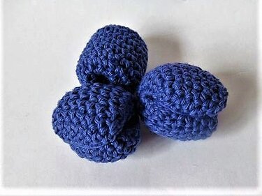 Drei dunkelblaue, gehäkelte Blaubeeren auf hellem Hintergrund