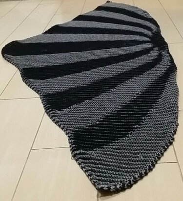 Asymmetrisches handgestricktes Tuch in Schwarz und Grau mit fächerförmigen Streifen auf hellem Fliesenboden