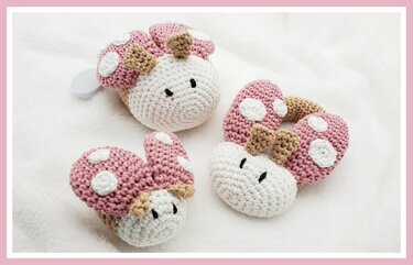Drei gehäkelte Babyspielzeuge in Rosa und Weiß mit weißen Punkten auf hellem Stoff