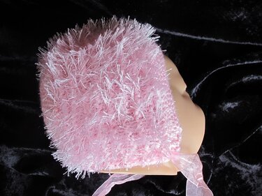 Rosa gestrickte Babyhaube aus flauschigem Garn mit Bindebändern auf einem Schaufensterkopf