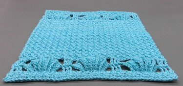 Hellblaues gehäkeltes Rechteck mit Noppenbordüre auf grauem Hintergrund