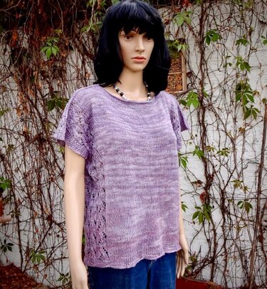 Schaufenstermannequin trägt lila gestricktes Kurzarm-Shirt mit Ajourmuster an den Seiten vor einer efeubewachsenen Wand