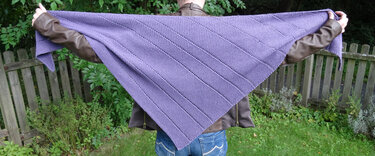 Großes gestricktes Dreieckstuch in Lila mit kraus-rechts-Muster und Reihen aus Löchern, gehalten von hinten