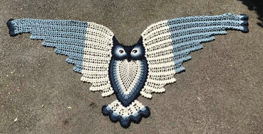 Blue and cream crochet owl triangle shawl laid flat on pavement.