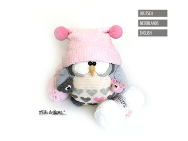 Crocheted owl amigurumi with pink pom-pom hat, heart-patterned belly, gray wings, small pig accessory and yarn skeins