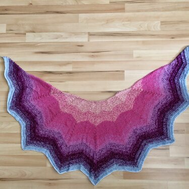 Halbrundes gestricktes Tuch mit Farbverlauf von Pink zu Blau auf hellem Holzboden