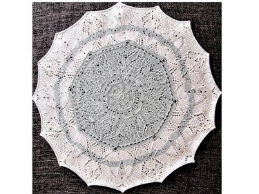 Rundes weißes gestricktes Deckchen mit gezackter Spitzenkante auf dunklem Untergrund