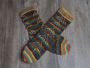 Bunte, gestrickte Socken mit schmalen Streifen und diagonalem Ajourmuster auf Holzuntergrund
