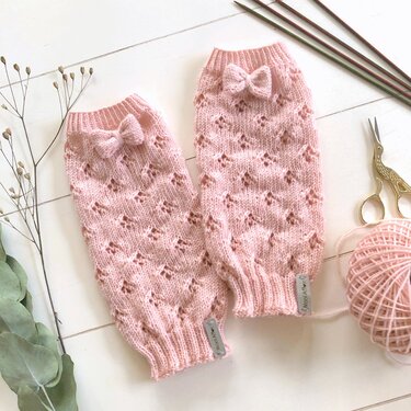 Pair of pastel pink knitted legwarmers with eyelet lace pattern and small bows