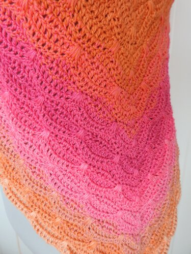 Close-up of a triangle crochet shawl with pink-to-orange gradient and chevron texture